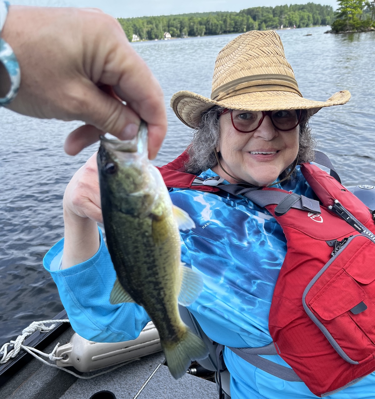 Marcia in a life vest, the fish she caught in the foreground, and the lake in the background.